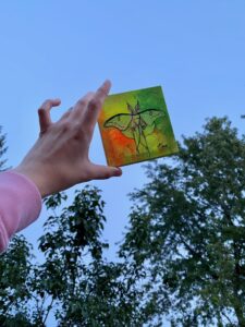 Hand holding up a small fluorescent painting of a luna moth. 