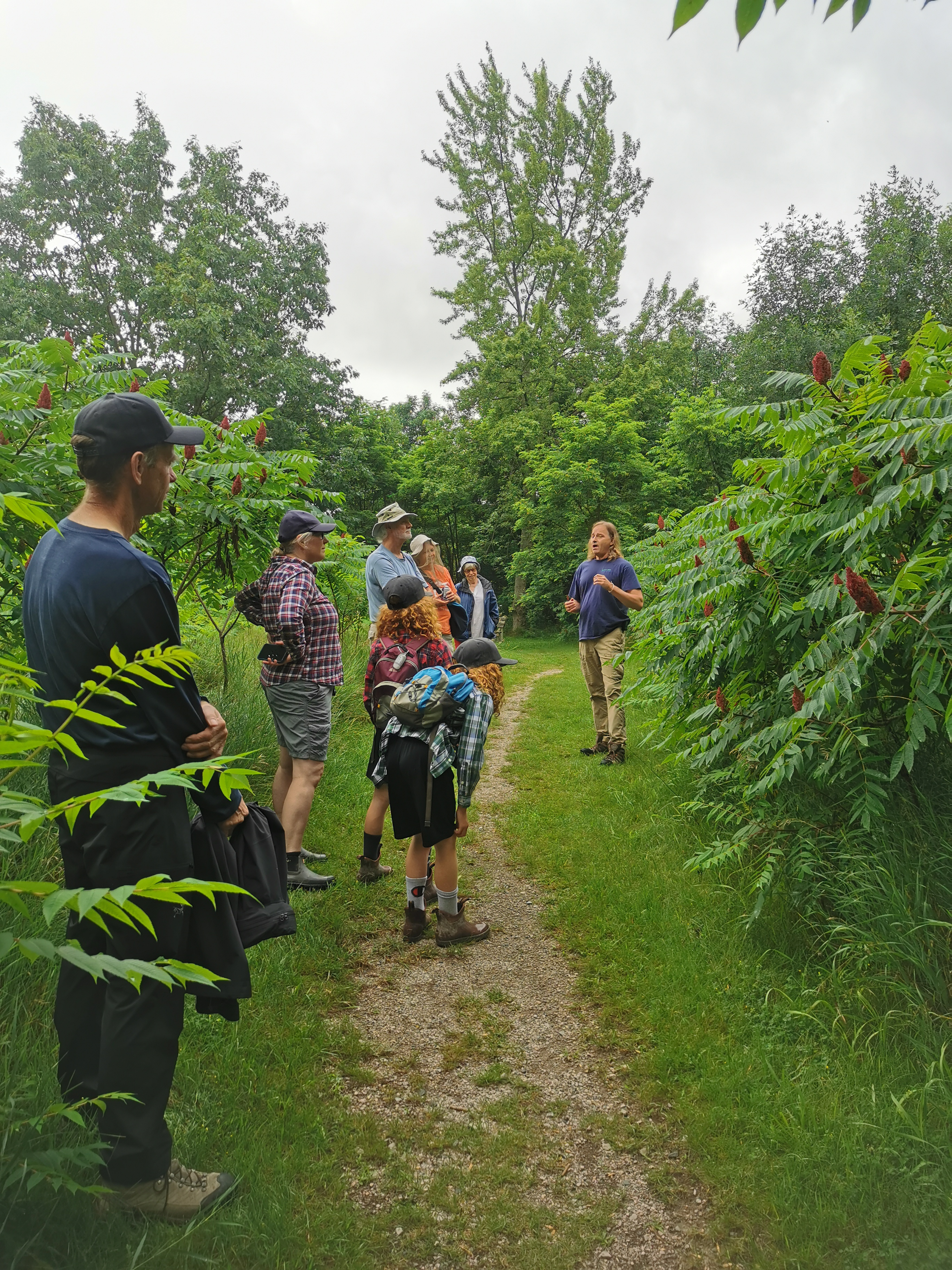 An educator guides a group of people on a walk along a treelined path.