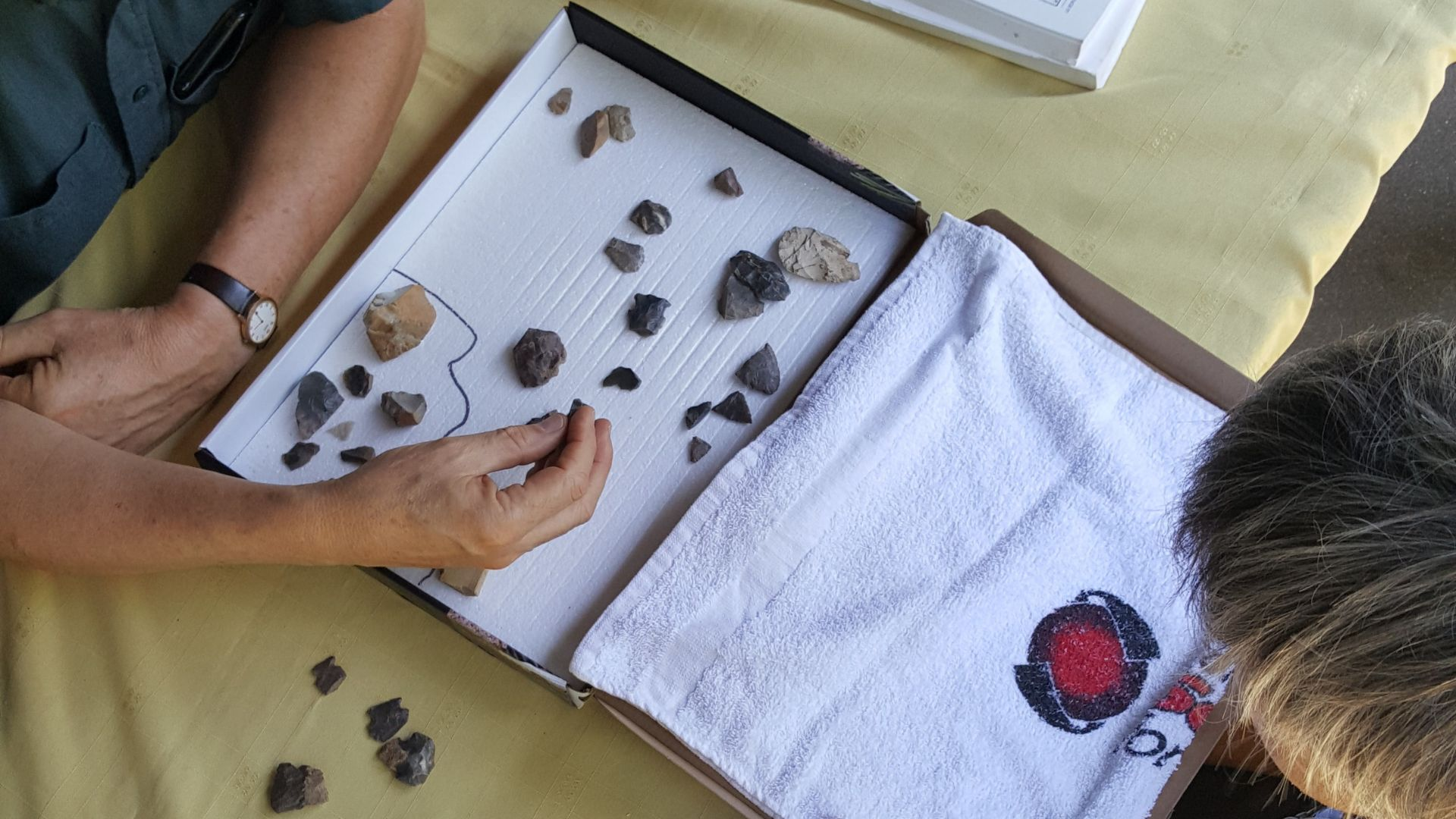 Close-up overhead of two people looking at stone artifacts in a box.