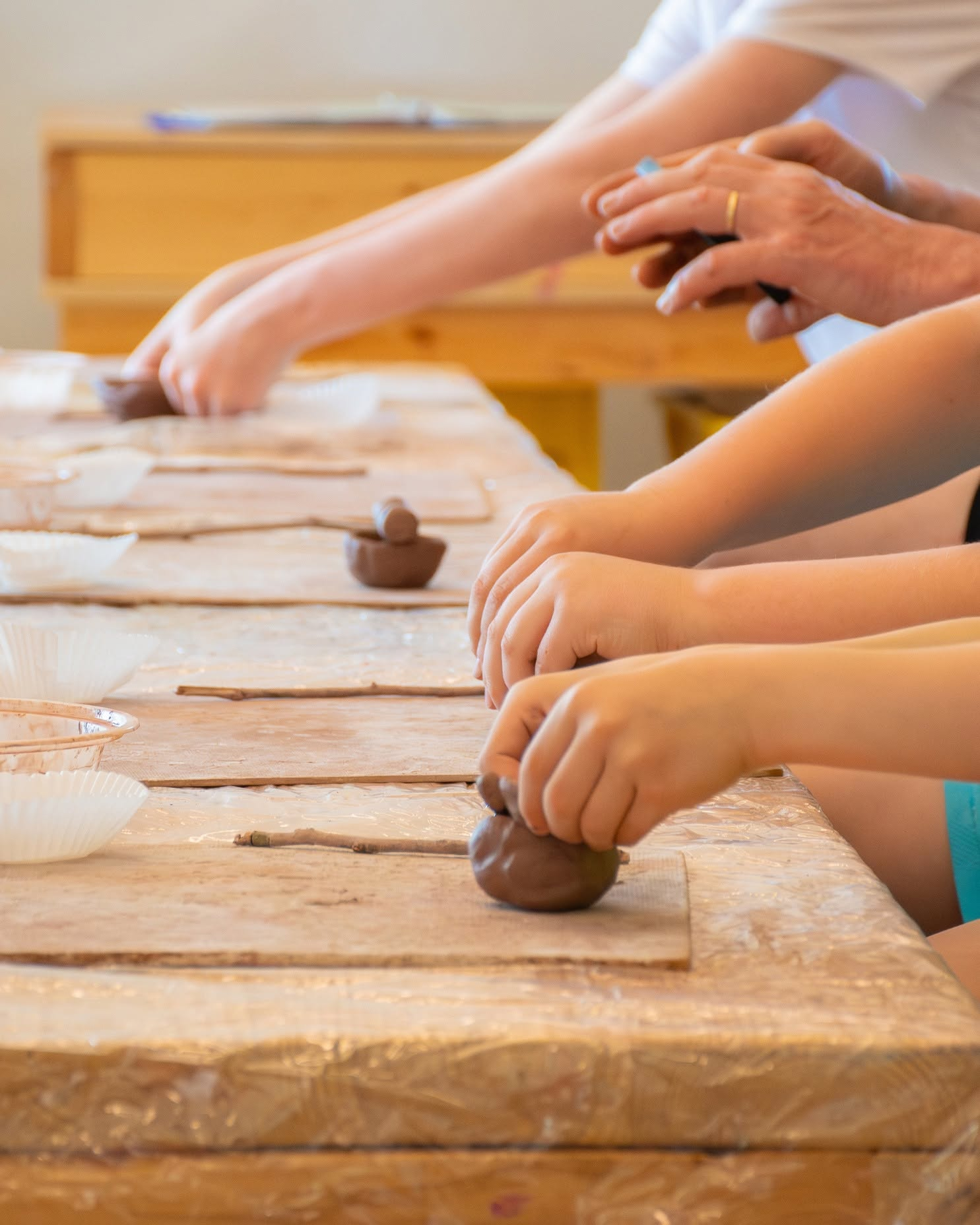 Hands making clay creations on a table covered in paper and wooden boards.